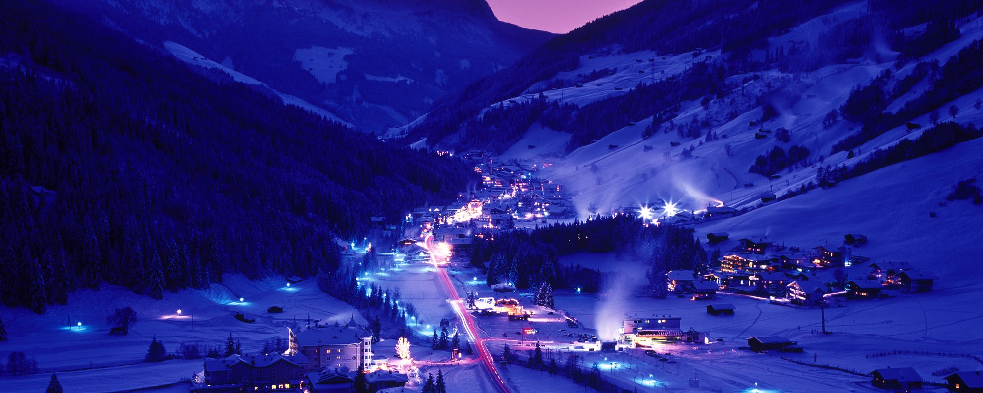 Spektakuläre Nachtaufnahme des tief verschneiten Winterdorfes Gerlos mit violetter Lichtstimmung und bei Vollmond